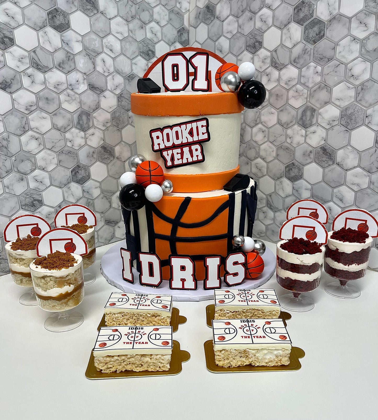 Basketball-themed birthday cake with smaller cakes and desserts on a hexagonal patterned wall background.